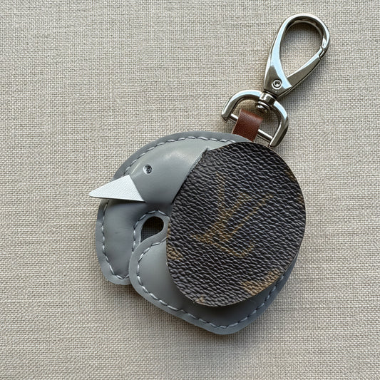 A handmade anrtisan crafted elephant-shaped keychain bag charm in gray and upcycled luxury brown monogram canvas, featuring a silver-tone lobster clasp, photographed on a textured linen background.